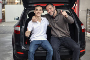 Father and son sitting and bonding on a car trunk. About 45 years old father and a 18 years old teenage son, both Caucasian male.
