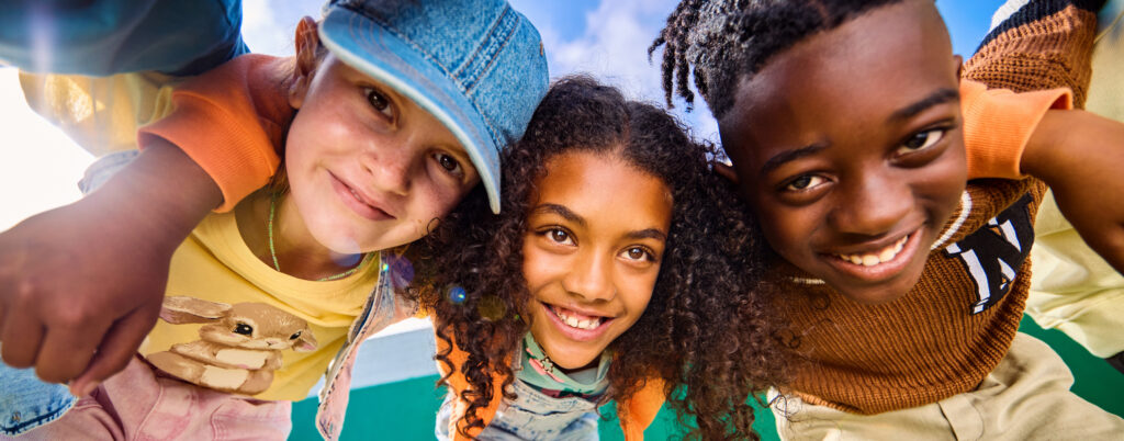 Happy multi-ethnic classmates are hugging each other in the schoolyard, smiling at the camera