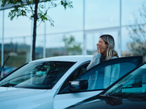 Exhausted woman yawning while entering her car on the street. Photographed in medium format.