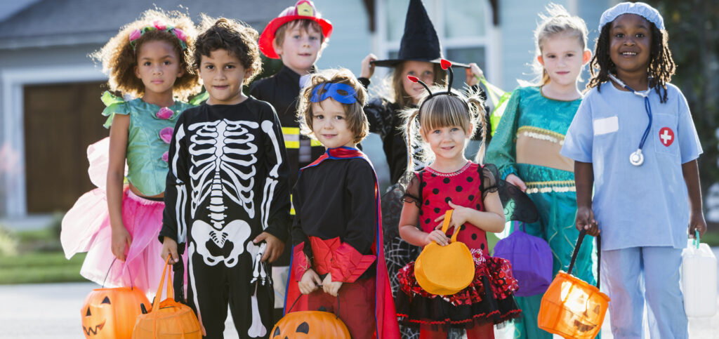 Multi-ethnic group of children 3-6 years old, wearing halloween costumes, ready to go trick or treating, standing in street in front of house.
