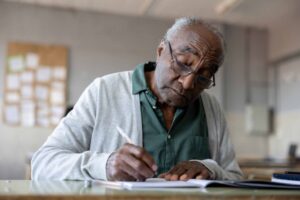 African American senior man studying in college and writing on his notebook in the classroom - education concepts