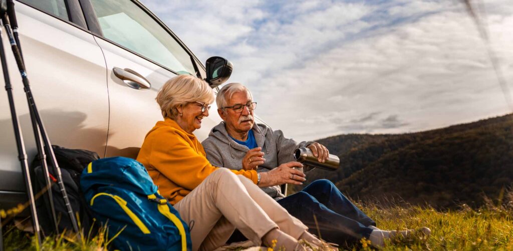 Senior couple sitting against the car, resting after hiking in countryside.