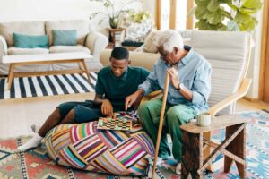 An elderly man and two children play checkers on a colorful pouf, capturing laughter, legacy, and intergenerational connection.