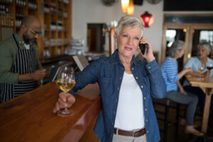 Senior woman talking on mobile phone while having glass of wine at counter in bar