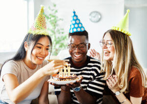 Group of young happy people friends having fun blowing candles on a birthday cake at home