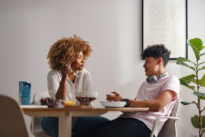 A candid moment captured as a mother and her teenage son share a meaningful conversation over breakfast in a light-filled dining room.