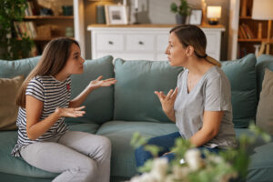 Mother and her teenage daughter are having a serious argument while sitting on the sofa in their living room