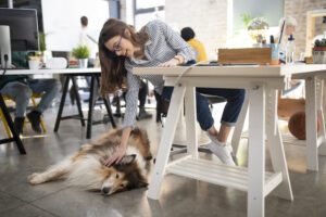 Young businesswoman working at the pet friendly office and cuddling her dog.
