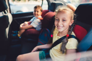 Brother and sister sitting at car safety seats and smiling to camera