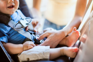 A mom buckles her infant son safely into a rear facing car seat as they get ready to drive somewhere in their vehicle. The baby's mouth is visible with a big smile. Sunlight shines in from behind. Horizontal with copy space.