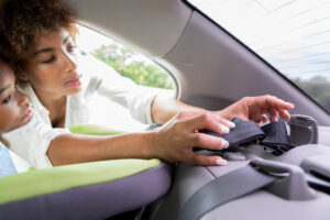 Young African American mom adjusts the seat belt before strapping her young daughter into a booster seat.